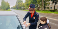 Полицейский инспектор прикрепляет белый бантик к автомобилю; рядом школьница с белым бантом в косе, городской жилой фон (дома, деревья, дорога). - 168.Ru