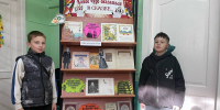 Книжная выставка на стеллаже с книгами Сергея Аксакова в детском отделе библиотеки; рядом два мальчика у стойки экспозиции. - 168.Ru