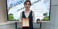 ученик в жилете держит диплом и приз на фоне большого экрана с картой и надписью «1000 маршрутов» и указанием областного фестиваля - 168.Ru