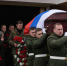 Военные несут гроб, покрытый российским флагом; рядом скорбящие люди с цветами и венком. - 168.Ru
