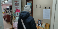 Интерьер библиотеки: на столе выставлены резные деревянные панно; посетители стоят спиной, вид со входа в читальный зал. - 168.Ru