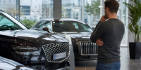 Мужчина осматривает два чёрных премиальных автомобиля в автосалоне. - 168.Ru