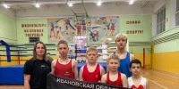 Группа молодых боксёров и тренер на фоне ринга держат флаг с надписью «Ивановская область / Кинешма» в спортивном зале. - 168.Ru