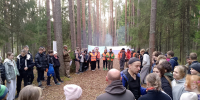 Группа подростков и взрослых в лесу на открытом мероприятии: кадеты и руководители выстроены по краям тропы, видны организаторы в оранжевых жилетах и баннер на фоне. - 168.Ru